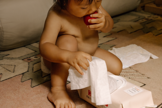 Baby eating an apple and playing with Huggies® Skin Essentials™ baby wipes